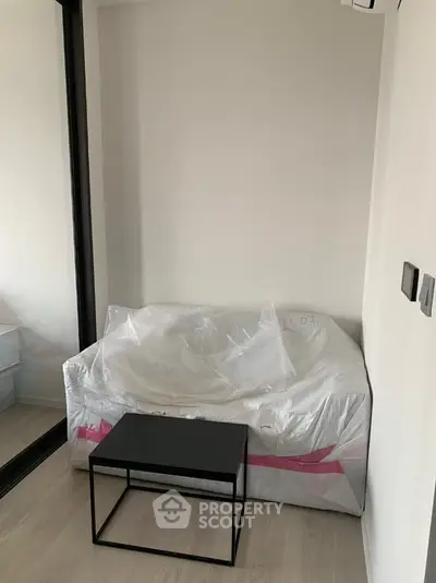 Modern minimalist bedroom with a sleek black table and bed wrapped in plastic.