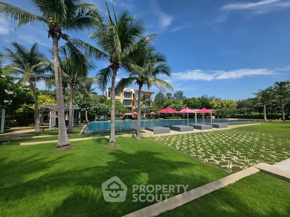 Luxurious resort-style garden with pool and palm trees under a clear blue sky.