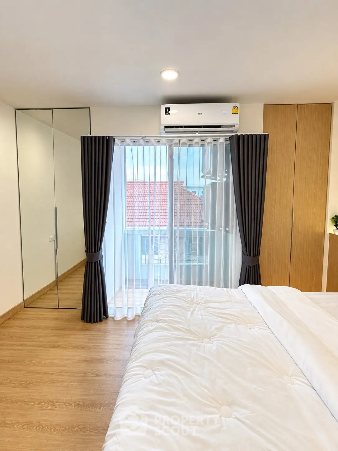 Bright and modern bedroom with balcony access and air conditioning, featuring wooden flooring and ample natural light.