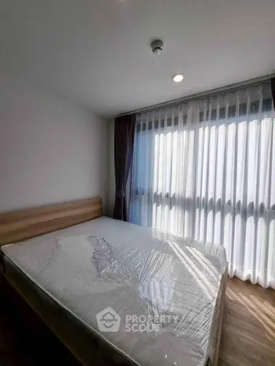 Modern bedroom with large window and natural light, featuring a new mattress and stylish curtains.