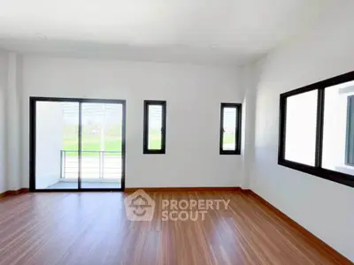 Spacious room with large windows and balcony access, featuring elegant wooden flooring.