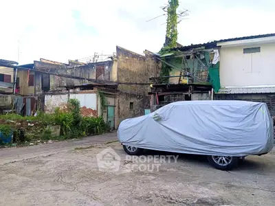 Dilapidated building exterior with covered car in foreground, potential for renovation.
