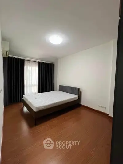 Spacious bedroom with wooden flooring and large window, perfect for natural light.