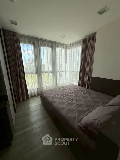 Modern bedroom with large windows and city view, featuring elegant curtains and stylish bedding.