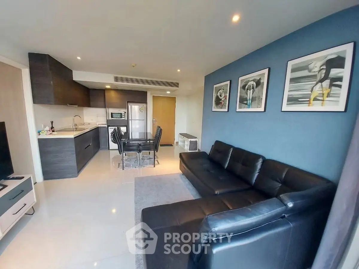 Modern living room with sleek black leather sofa and stylish kitchen in open layout apartment.