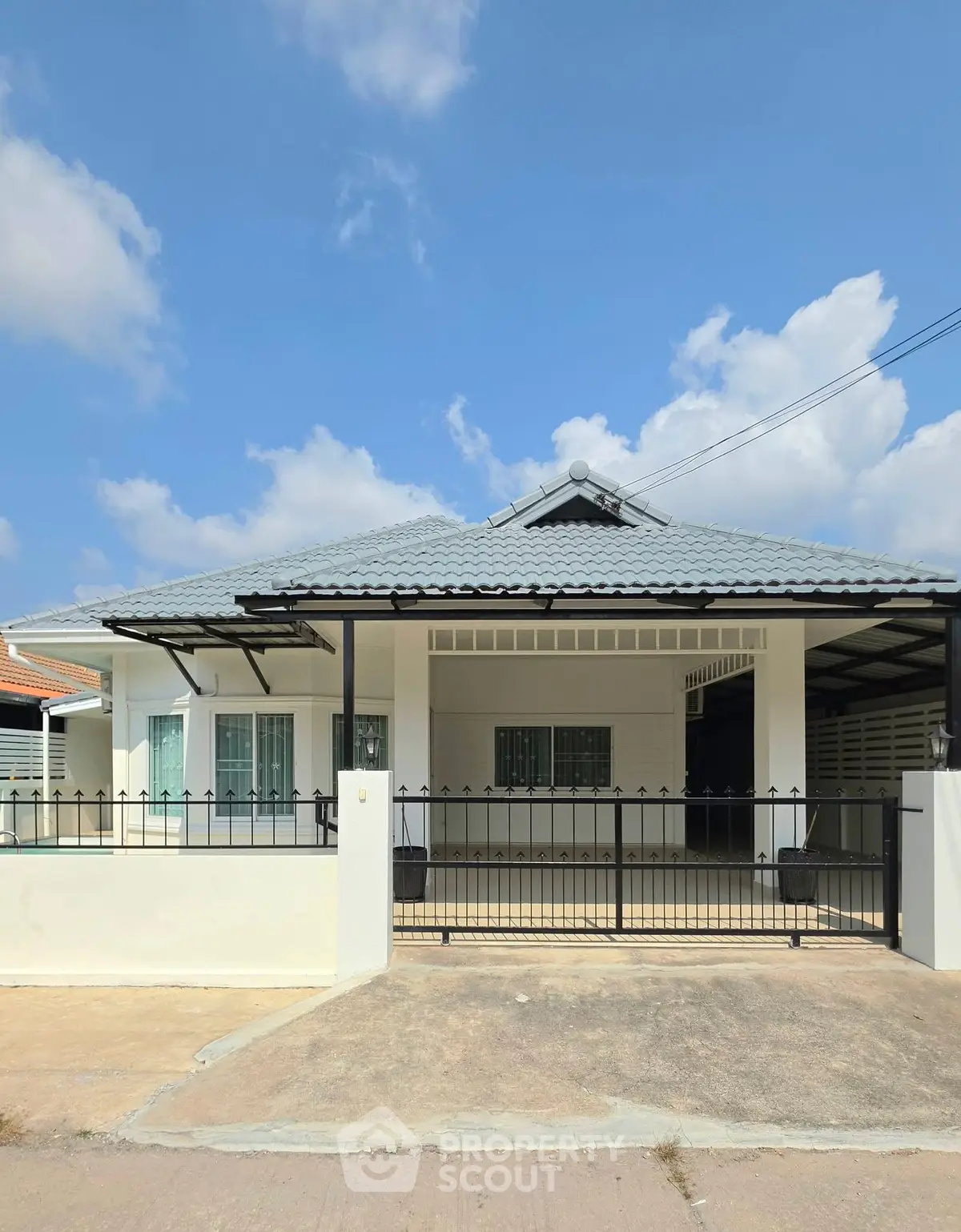 Charming single-story house with a modern roof and gated driveway under a clear blue sky.