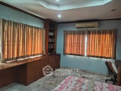 Spacious study room with built-in desk and shelves, featuring large windows with curtains and air conditioning.