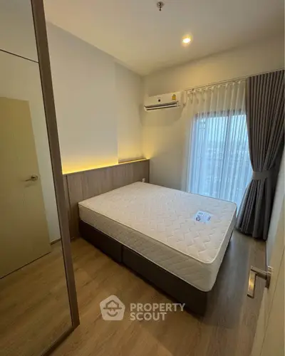 Modern bedroom with minimalist design, featuring a large window and air conditioning unit.