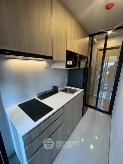 Modern compact kitchen with sleek cabinetry and induction cooktop in a stylish apartment.