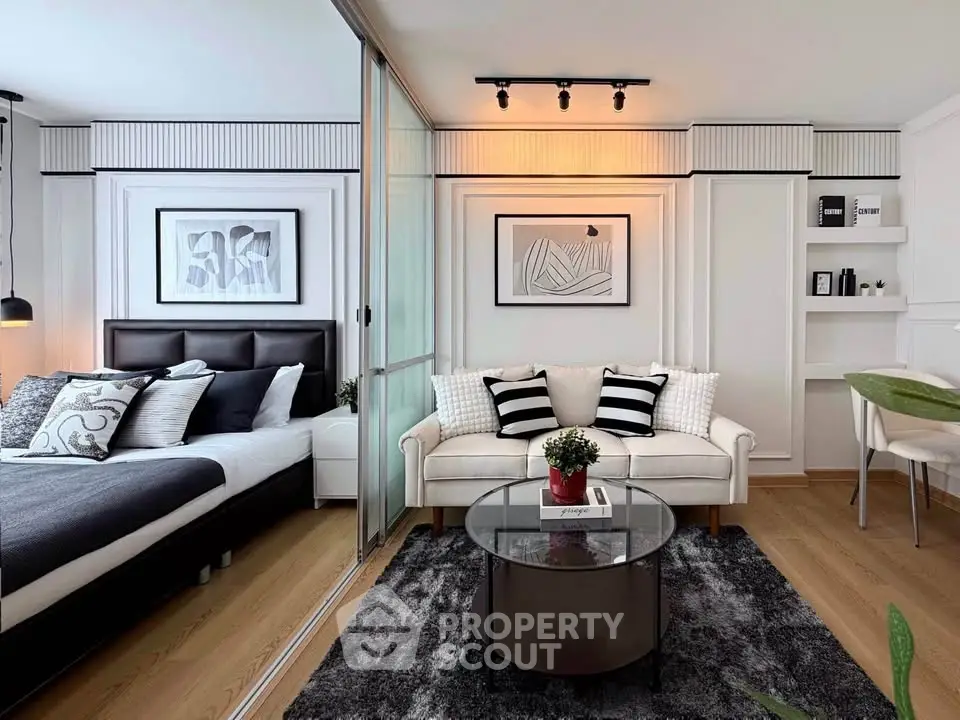 Modern living room with stylish decor and cozy bedroom separated by glass partition.