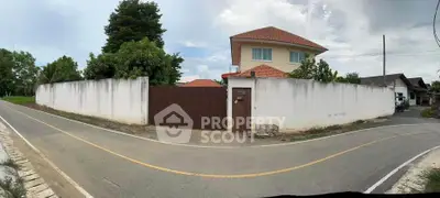 Charming suburban house with red roof and white walls, surrounded by lush greenery and a secure wooden gate.