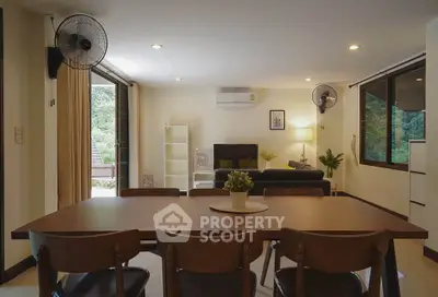 Spacious living room with modern decor and large windows offering natural light and greenery views.