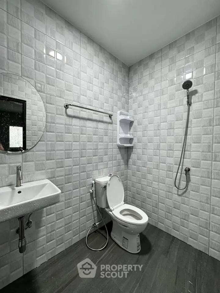 Modern bathroom with sleek fixtures and tiled walls, featuring a round mirror and handheld shower.