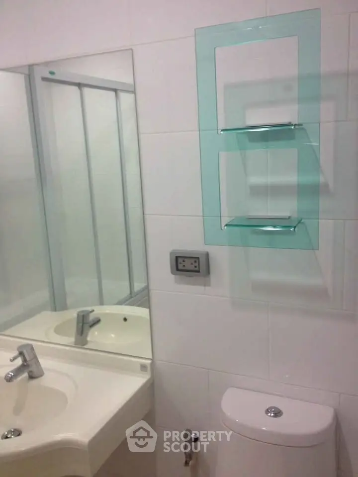 Modern bathroom with sleek fixtures and glass shelving in a contemporary apartment.