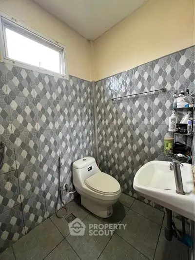 Compact bathroom with modern fixtures and patterned tile walls, featuring a toilet and sink.