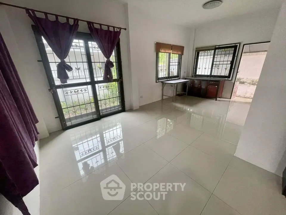 Spacious living room with glossy tiled flooring, large windows with burgundy curtains, and ample natural light, perfect for family gatherings.