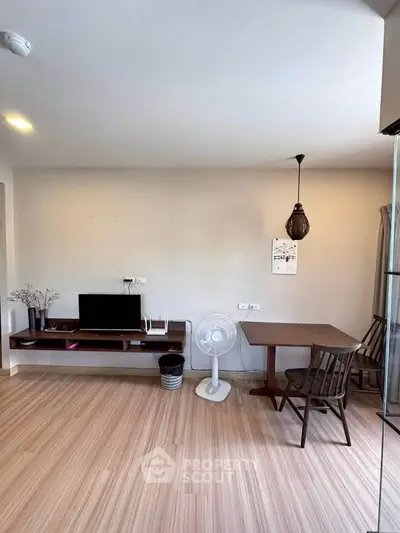 Modern living room with wooden flooring, TV setup, and dining area in a cozy apartment.