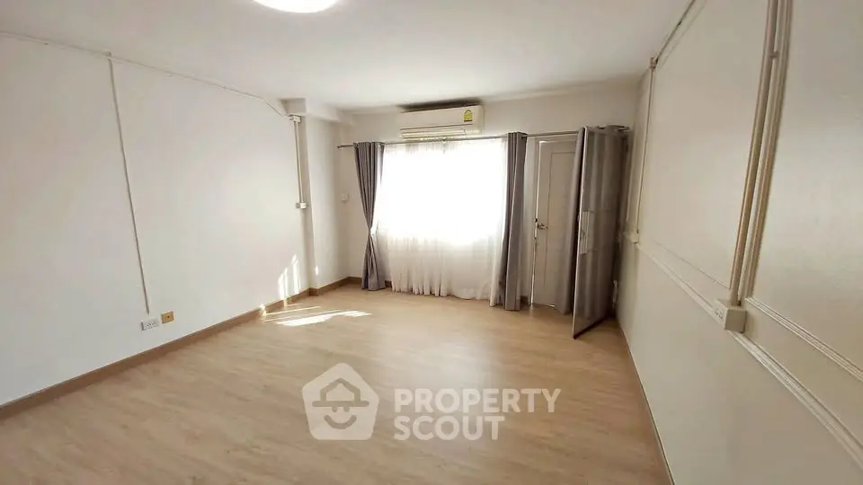 Spacious empty room with wooden flooring and large window, perfect for customization.