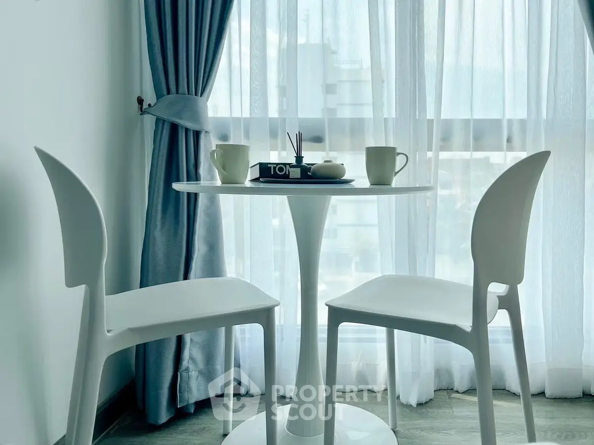 Chic modern dining nook with elegant white chairs and table by a sunlit window.