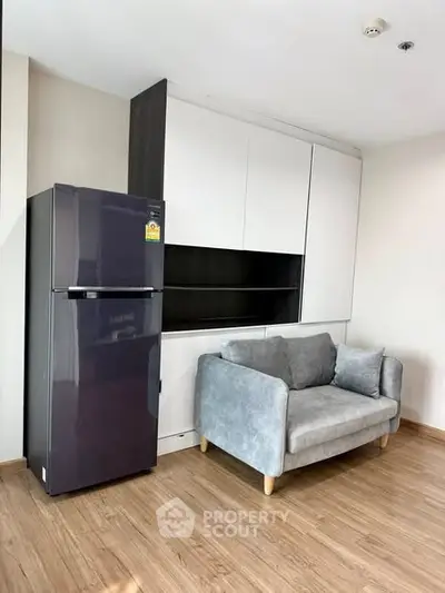 Modern apartment interior with sleek fridge and cozy sofa on wooden flooring.