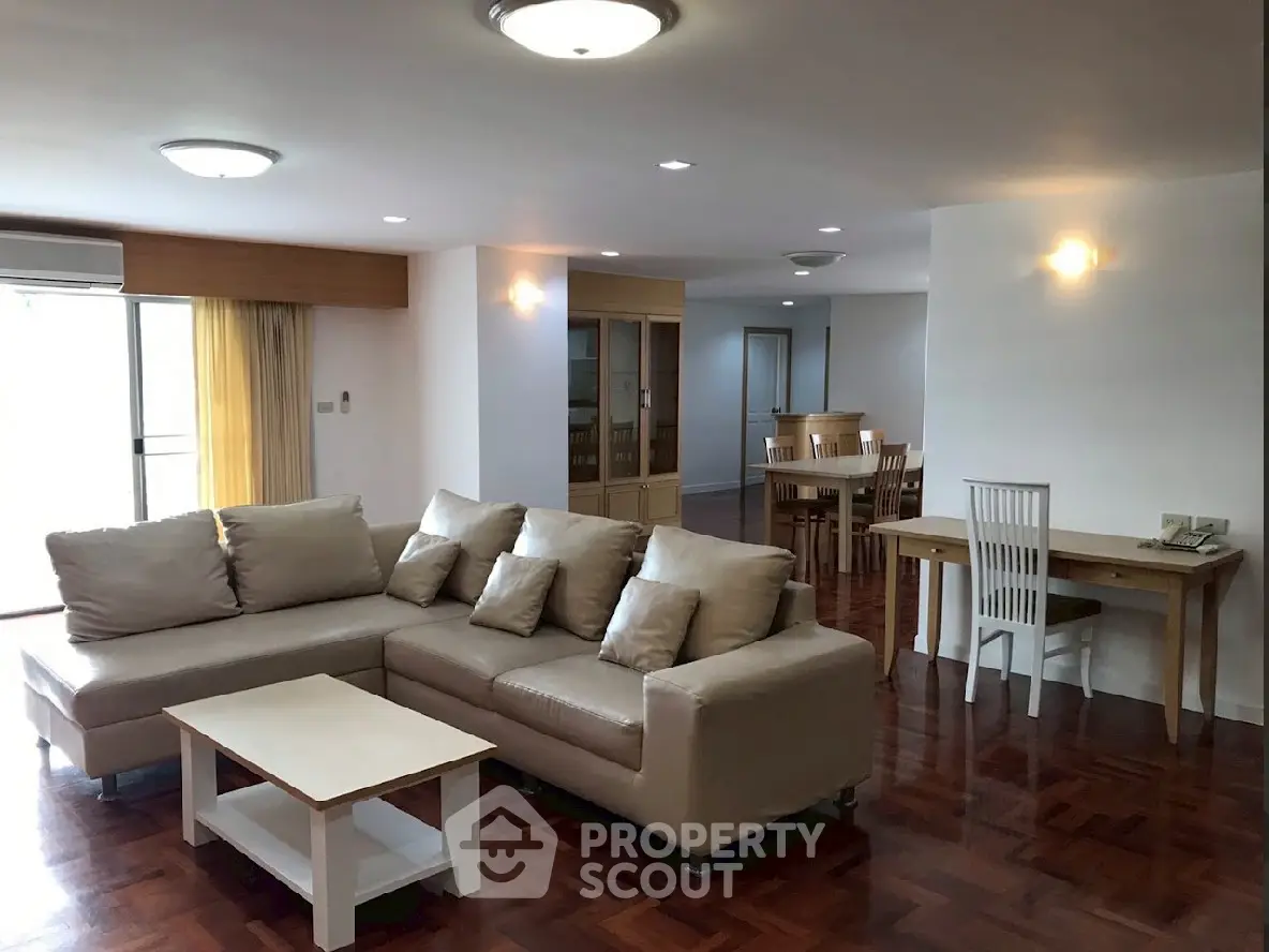 Spacious living room with modern furniture and dining area, featuring elegant wooden flooring.