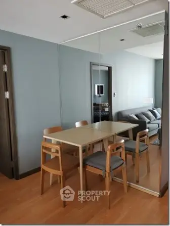 Modern dining area with wooden table and chairs, mirrored wall, and cozy living room view.