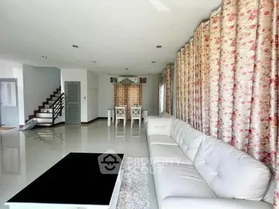 Spacious living room with elegant white sofa and floral curtains, perfect for modern family living.