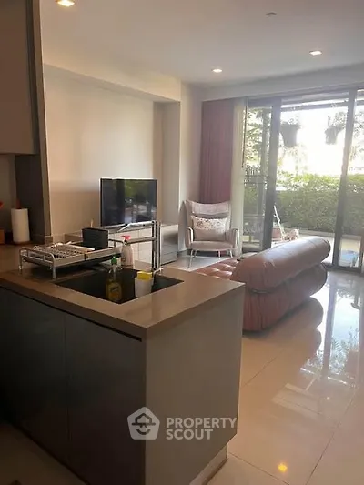 Modern living room with open kitchen and garden view, featuring sleek furniture and natural light.
