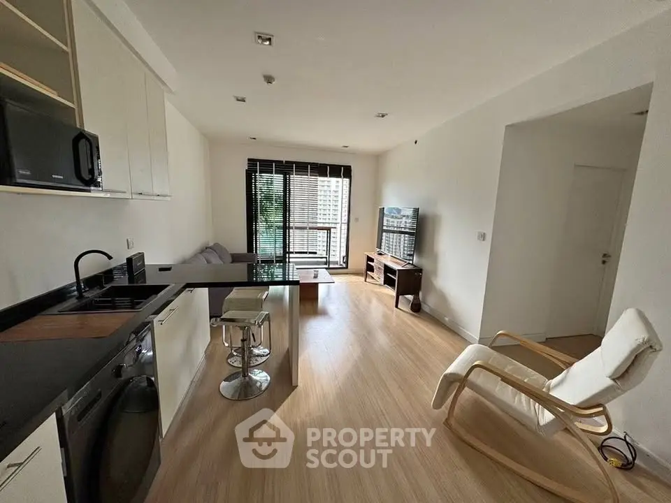 Modern open-layout living room with kitchen, featuring sleek furniture and natural light.