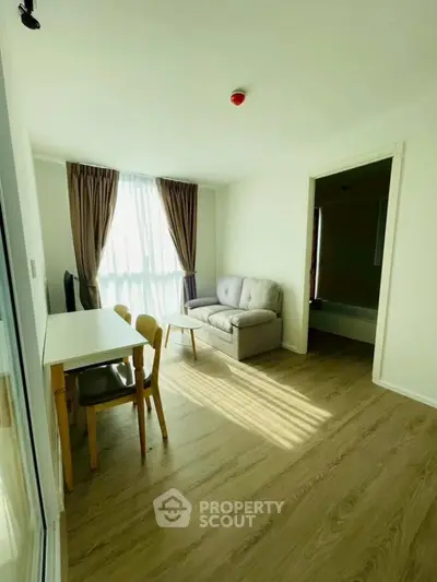 Bright living room with cozy sofa and dining area, featuring large window and wooden flooring.