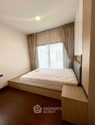 Spacious bedroom with large window and elegant curtains, featuring a built-in bed and wooden flooring.