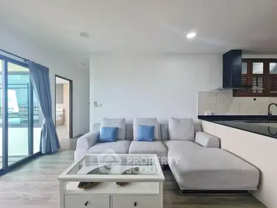 Modern living room with sectional sofa and glass coffee table, open to a sleek kitchen area.