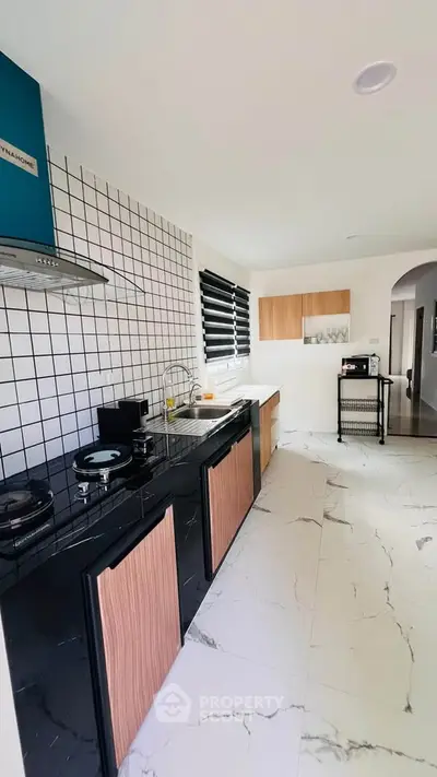 Modern kitchen with sleek black and wood cabinetry, tiled backsplash, and marble flooring.
