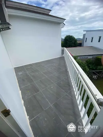 Spacious balcony with modern tiles and white railing overlooking lush greenery