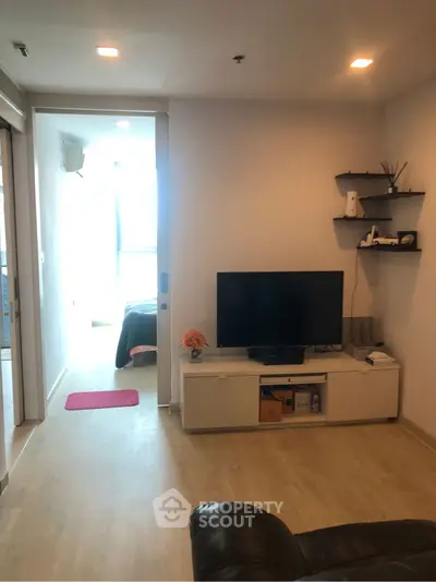 Cozy living room with modern decor and TV setup, leading to a bright bedroom.