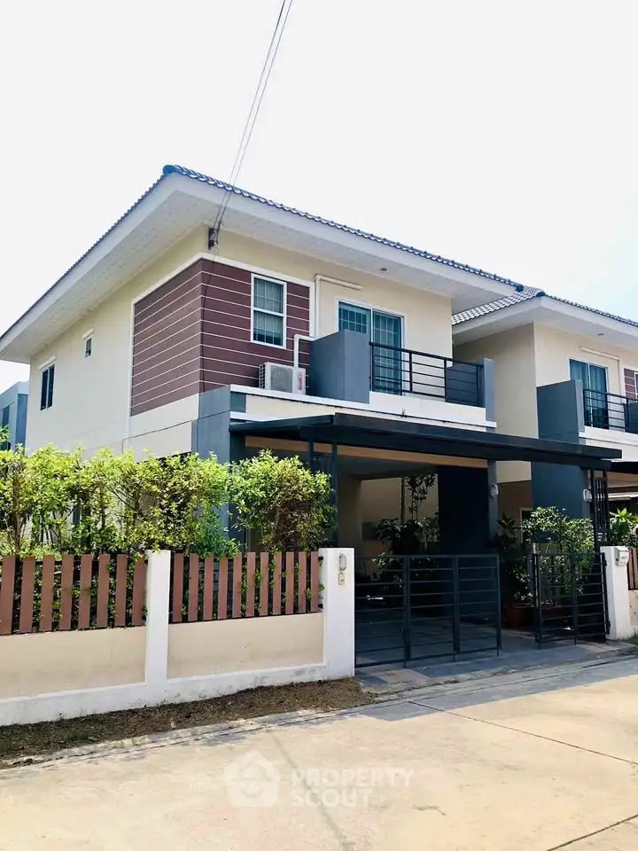 Modern two-story house with balcony and garden in a suburban neighborhood.