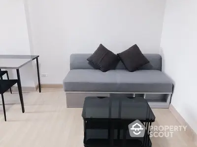 Modern minimalist living room with sleek grey sofa, black accent tables, and light wood flooring, ideal for urban living.