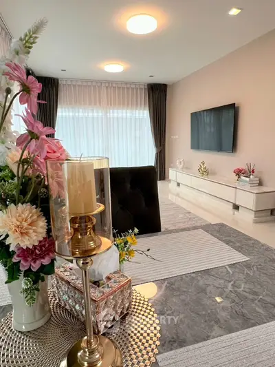 Elegant living room with modern decor and large TV, featuring stylish furniture and floral accents.