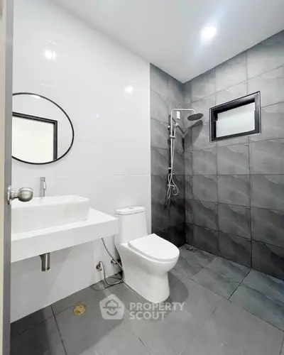 Modern bathroom with sleek design, featuring a round mirror, white sink, and stylish shower area.
