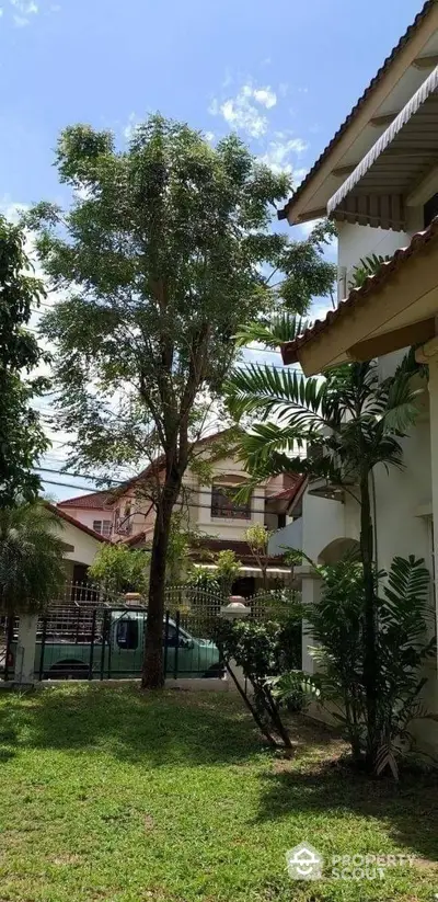 Lush green garden with mature tree enhancing the curb appeal of this charming two-story residence, complete with a spacious lawn and tropical foliage.