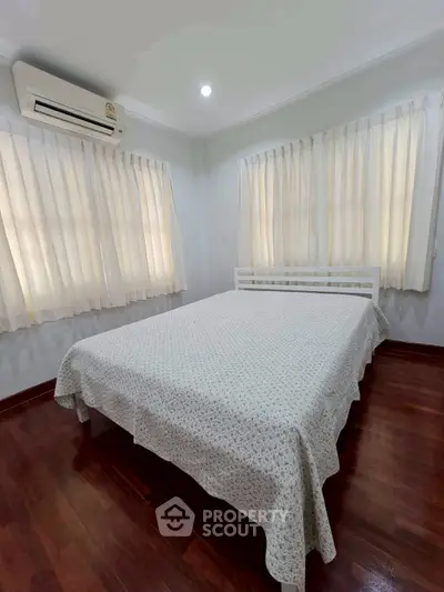 Cozy bedroom with wooden flooring and ample natural light from large windows.