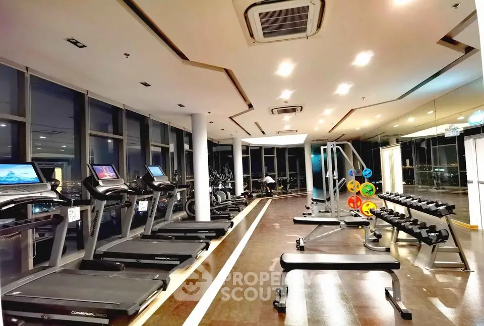 Modern gym with treadmills, weights, and panoramic city views in luxury apartment building.