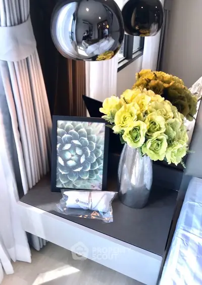 Elegant bedroom corner with modern decor, featuring a stylish vase of flowers and framed artwork on a sleek table.