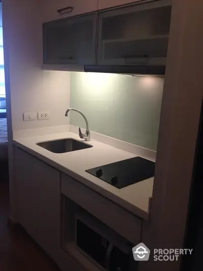 Modern compact kitchen with sleek white cabinetry, built-in oven, and a stylish glass cooktop, perfect for urban living.