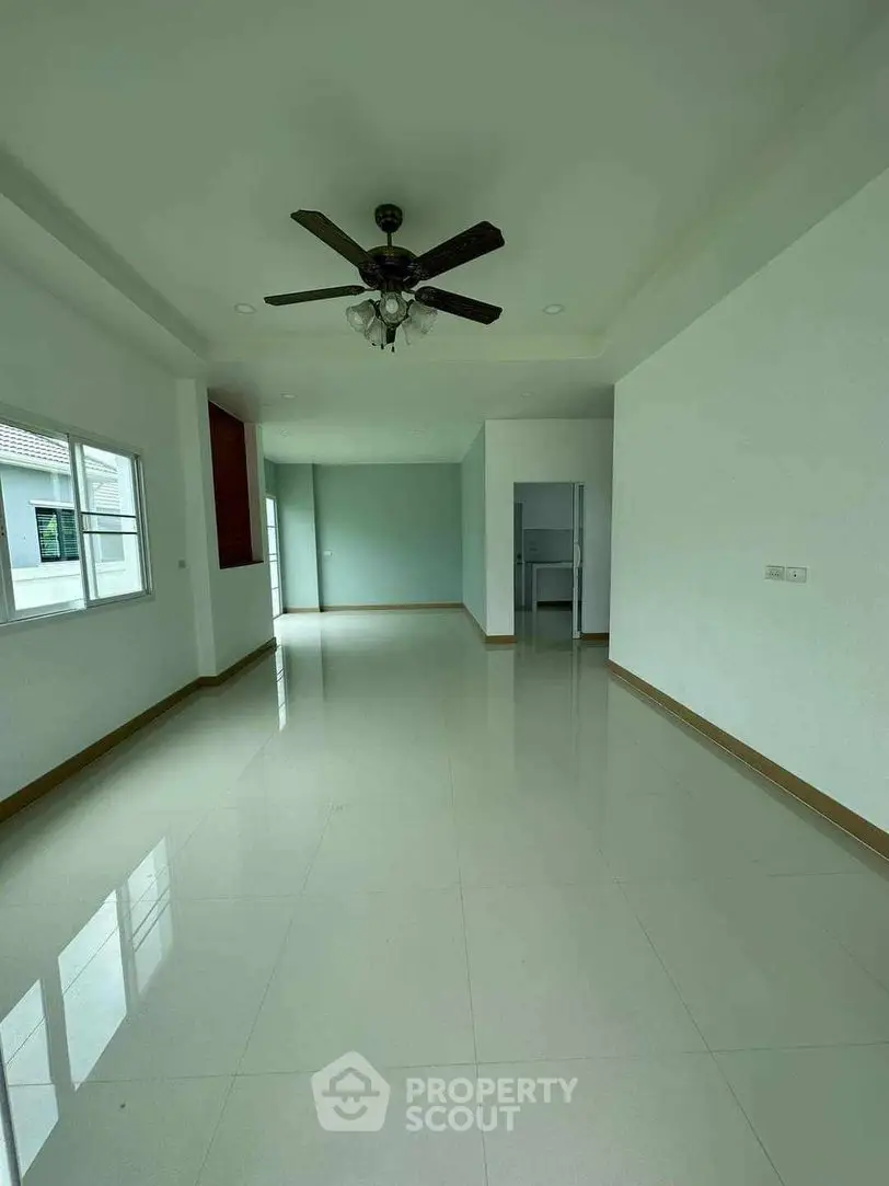 Spacious and well-lit living area with glossy tiled flooring, elegant ceiling fan, and a seamless transition to a modern kitchen, perfect for entertaining and comfortable living.
