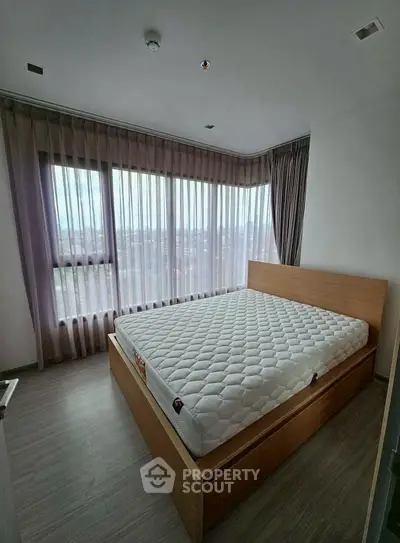 Spacious bedroom with large windows and modern design, featuring a comfortable bed and elegant curtains.