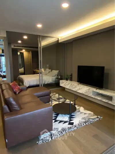 Modern living room with leather sofa, TV, and stylish decor leading to a cozy bedroom.