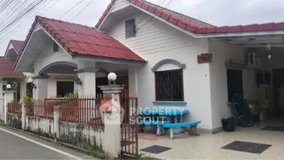 Charming single-story house with red roof and fenced yard, featuring a cozy outdoor seating area.