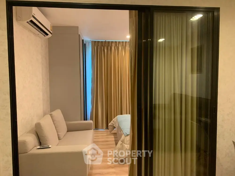 Modern apartment with sliding glass doors separating living and bedroom areas, featuring cozy sofa and elegant curtains.