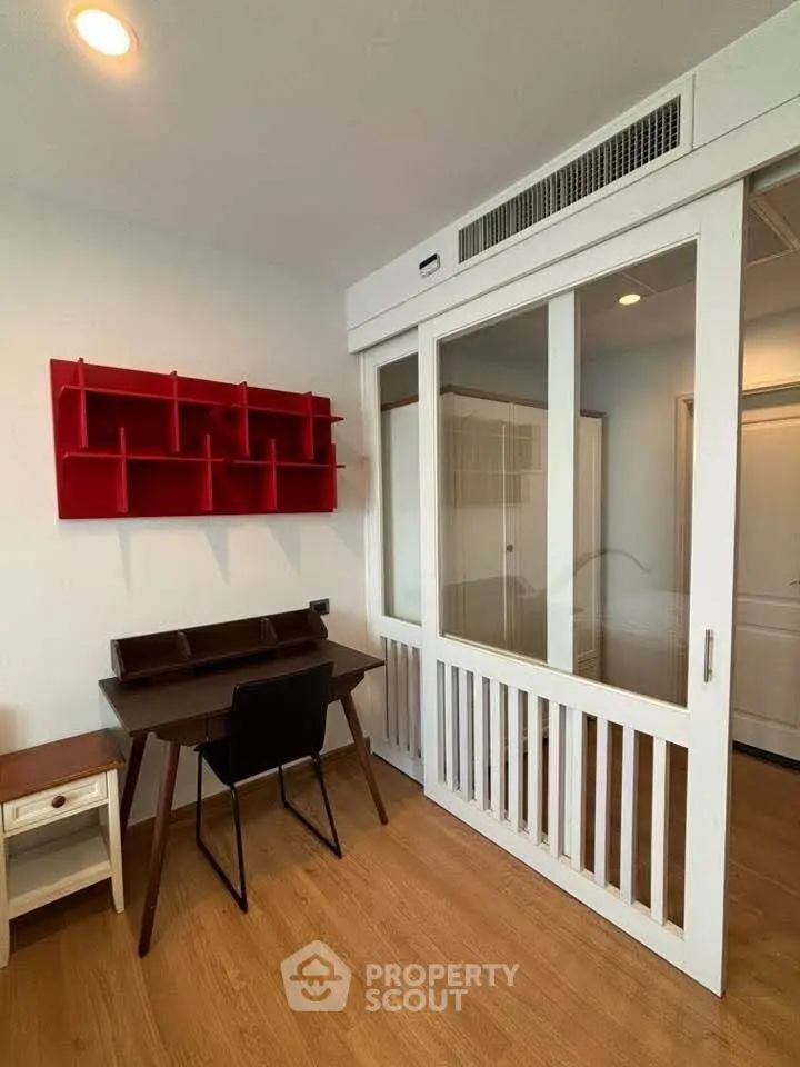 Modern study room with sleek desk and chair, featuring a red wall shelf and sliding glass doors.